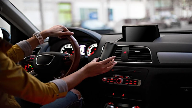 A man is driving a car and holding a car phone mount in his right hand