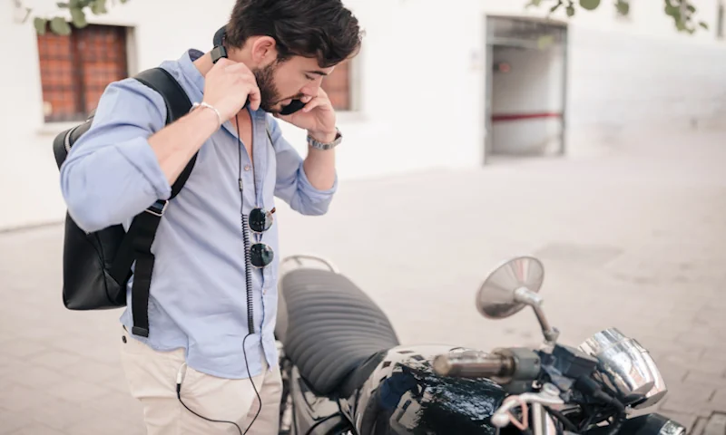 A man waring earbuds and listening phone near a motorcycle